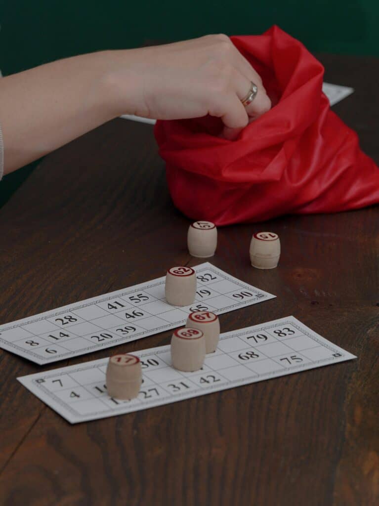 Hand reaching into red bag during wooden token bingo game on table.